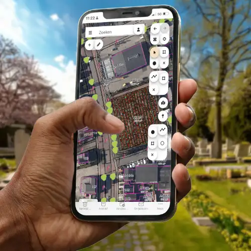 BAM digitale plattegrond Een medewerker begraafplaatsadministratie met een smartphone in de hand. Op de smartphone de digitale plattegrond module van BAM. Op de achtergrond een begraafplaats in de lente.